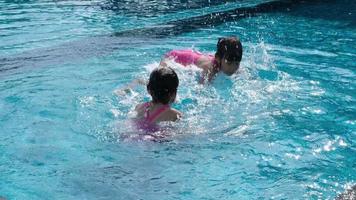 las hermanitas felices juegan en la piscina al aire libre del complejo tropical durante las vacaciones familiares de verano. niños aprendiendo a nadar. actividades saludables de verano para niños. video