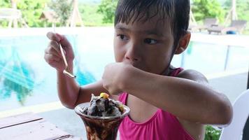 bagnato poco ragazza nel un' costume da bagno mangiare ghiaccio crema di il all'aperto piscina durante famiglia estate vacanza. estate stile di vita concetto. video