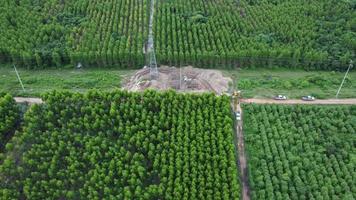 vista aérea de escavadeiras estão trabalhando nas fundações de postes de alta tensão e nas pernas de postes de alta tensão. vista superior da construção de linhas de energia na floresta. video