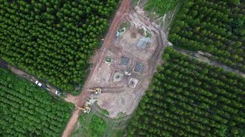 vista aérea de las excavadoras están trabajando en los cimientos de las torres de alta tensión y las patas de los postes de alta tensión. vista superior de la construcción de líneas eléctricas en el bosque. video