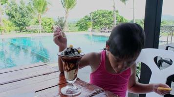 niña mojada en traje de baño comiendo helado junto a la piscina al aire libre durante las vacaciones familiares de verano. concepto de estilo de vida de verano. video