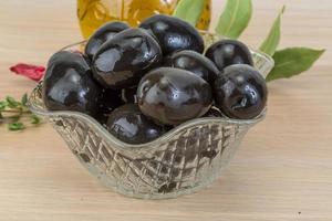 Black olives in a bowl on wooden background photo