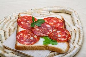 Sándwich de salami sobre tablero de madera y fondo de madera foto