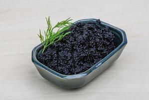 Black caviar in a bowl on wooden background photo