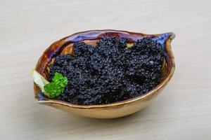 caviar negro en un recipiente sobre fondo de madera foto