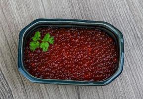 caviar rojo en un recipiente sobre fondo de madera foto