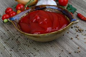 Tomato ketchup in a bowl on wooden background photo