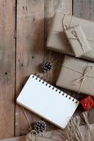 christmas gift box Use brown recycled paper and a notebook and pine cones on a wooden table. photo