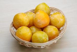 Yellow plums in a basket on wooden background photo