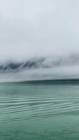 Fog floats among the mountain forest shore line as seen from boat video