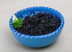 Black caviar in a bowl on wooden background photo