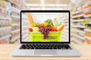 supermarket aisle blurred background with laptop computer and shopping basket on wood table grocery online concept photo