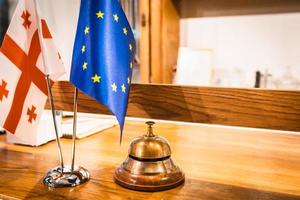 Ring bell on front desk in hotel with EU and georgian flag. Diplomatic relations and hospitality industry in caucasus and europe. Travel in world. photo