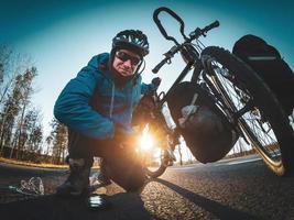 Cyclist on the side of the road posing for selfie and holding his bicycle with one hand and with accessories on the ground. Wide angle sports photography. photo