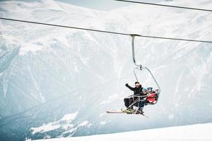 Gudauri, Georgia, 2022 - instructor with young kids on ski lift talk enjoy ride wave to photographer on ski lesson. Learning to ski on winter vacation on high caucasus mountains photo