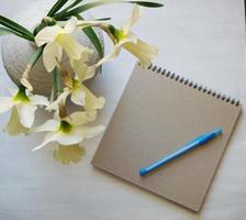 Notepad with pen, daffodils in a vase on a white table. Inspirational workplace. photo