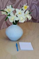 White daffodils in a vase on a table with with a notebook. photo