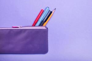 Fashionable violet pencil case with multicolored felt-tip pens, pencils and pens on violet background. photo