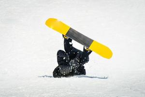 Male snowboarder on snowboard land on back in ski resort. Learning tricks and extreme ride downhill. Accidents on slopes in winter concept photo