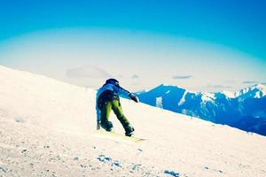 Un joven snowboarder desciende cuesta abajo en las pintorescas montañas del Cáucaso en un rápido movimiento de congelación empinado cuesta abajo en solitario foto