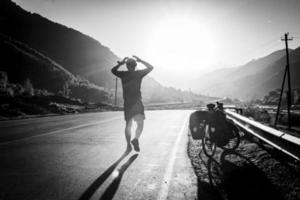 ciclista en bicicleta frustrado con las manos en la cabeza en las montañas mientras hacía cicloturismo. Estrés y miedos durante el viaje. imagen en blanco y negro. foto