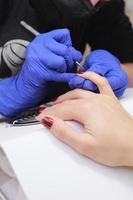 Master in protective mask and gloves during a manicure at beauty salon. Master manicurist varnishes the marsala gel on the nails of a female client. The concept of beauty and health. photo