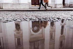 foto recortada de una feliz pareja joven y elegante, disfrutando de su abrazo en el viejo camino en la calle de la ciudad con un edificio antiguo en el fondo. Después de la lluvia. enfoque selectivo