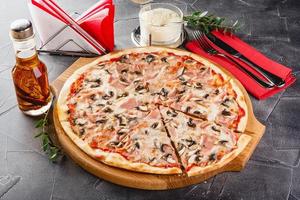 Pizza with ham and mushrooms on wooden board on dark background. Close-up photo