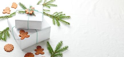 Christmas gifts wrapped in white paper and decorated with spruce sprigs and gingerbread cookies photo