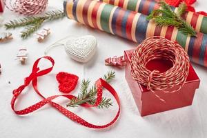 fondo de navidad con cajas de regalo, cinta, hilo, rollos de papel, corazones tejidos y adornos navideños.