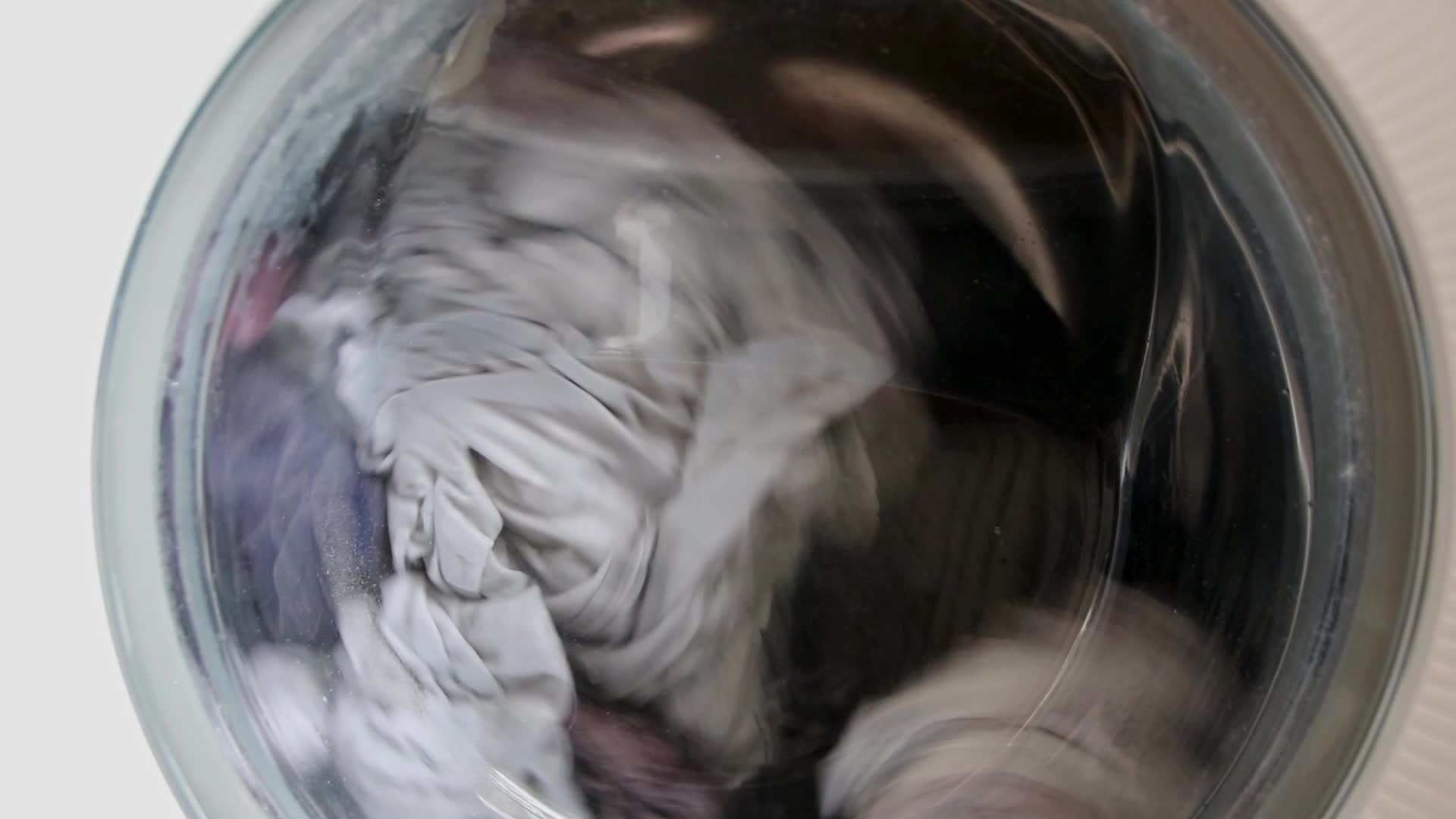 Dirty clothes in washing machine turning and cleaning the laundry with