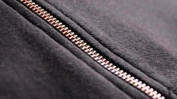 Copper colored fashion zipper in close-up macro view showing black sweatshirt with partial opened metal zipper with black fabric in metallic optic as elegant apparel or stylish fastener solid material