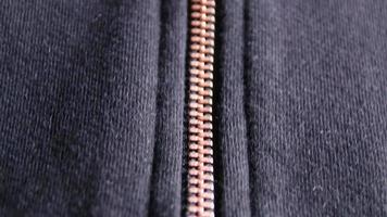 Copper colored fashion zipper in close-up macro view showing black sweatshirt with partial opened metal zipper with black fabric in metallic optic as elegant apparel or stylish fastener solid material video