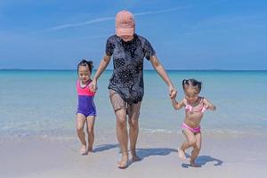 Happy Asian family consisting of a mother and two daughters having fun playing beach in summer vacation on the beach. Happy family, Holiday travel, and vacation concept. photo