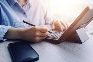 Businessman hands working with finances about cost and calculator and laptop with tablet, smartphone at office in morning light photo