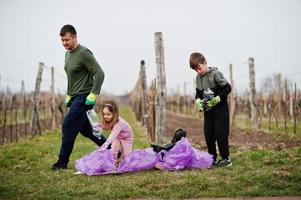 Family with trash bag collecting garbage while cleaning in the vineyards . Environmental conservation and ecology, recycling. photo