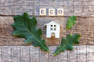 Miniature toy model house with inscription ECO letters word on wooden background photo