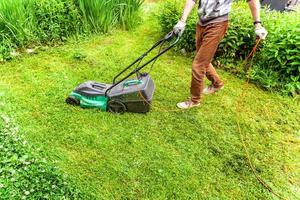 Man cutting green grass with lawn mower in backyard. Gardening country lifestyle background. Beautiful view on fresh green grass lawn in sunlight, garden landscape in spring or summer season. photo