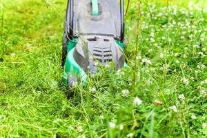 Man cutting green grass with lawn mower in backyard. Gardening country lifestyle background. Beautiful view on fresh green grass lawn in sunlight, garden landscape in spring or summer season. photo