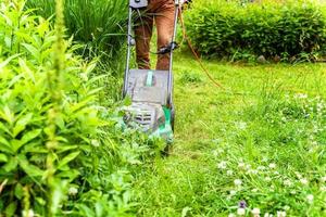 Man cutting green grass with lawn mower in backyard. Gardening country lifestyle background. Beautiful view on fresh green grass lawn in sunlight, garden landscape in spring or summer season. photo