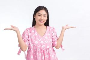 linda chica asiática con una camisa rosa sonriendo y mostrando la mano para presentar algo sobre un fondo blanco.