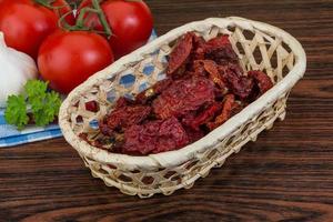 Dried tomtoes in a basket on wooden background photo