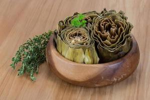 Boiled artichokes in a bowl on wooden background photo