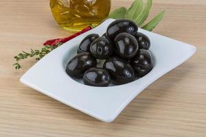 Black olives in a bowl on wooden background photo