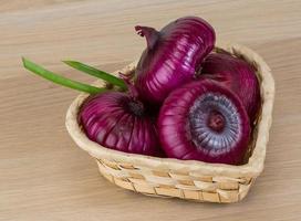 cebolla violeta en una cesta sobre fondo de madera foto