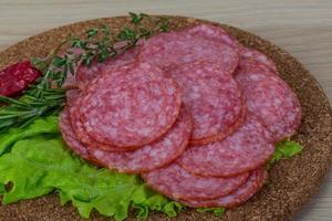 salami en rodajas sobre tablero de madera y fondo de madera foto