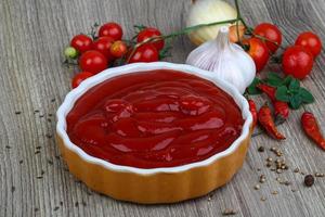 Tomato ketchup in a bowl on wooden background photo