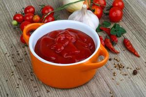 Tomato ketchup in a bowl on wooden background photo