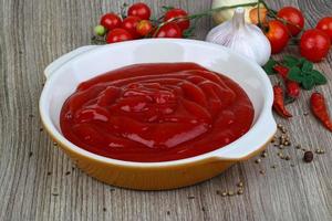 Tomato ketchup in a bowl on wooden background photo