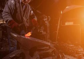 herrero forja manualmente el metal fundido con la luz del sol a través de las ventanas foto
